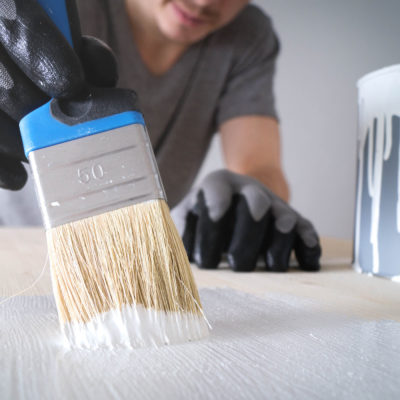 close-up: brush with white paint on a wooden table and a jar with white paint